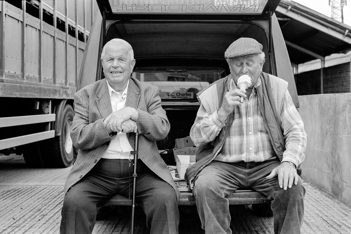 Two farmers, one eating ice cream, enjoying a break at the old Hereford Cattle Market