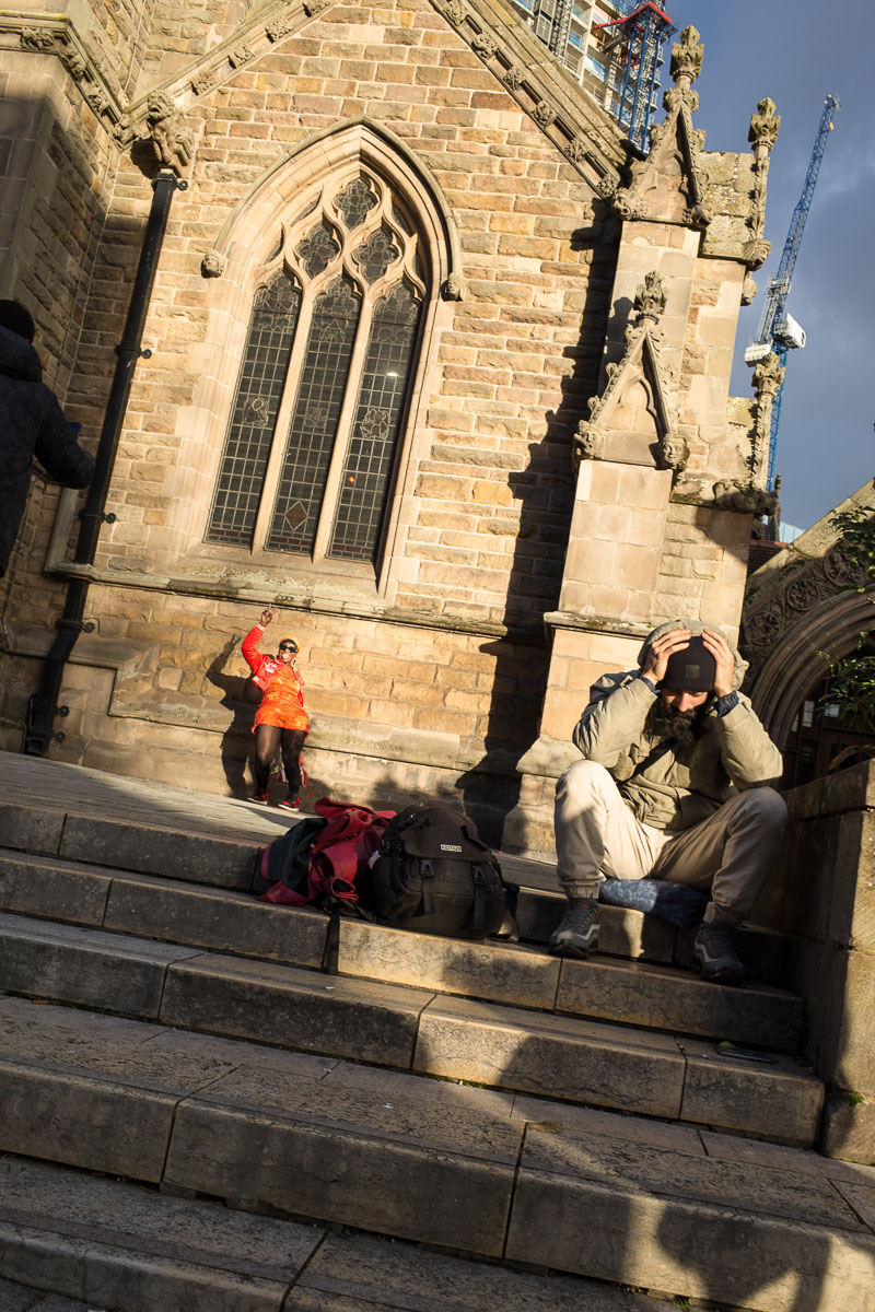 A woman poses for photos, as a man rests on the steps outside St. Martin's Church—a street photography scene.
