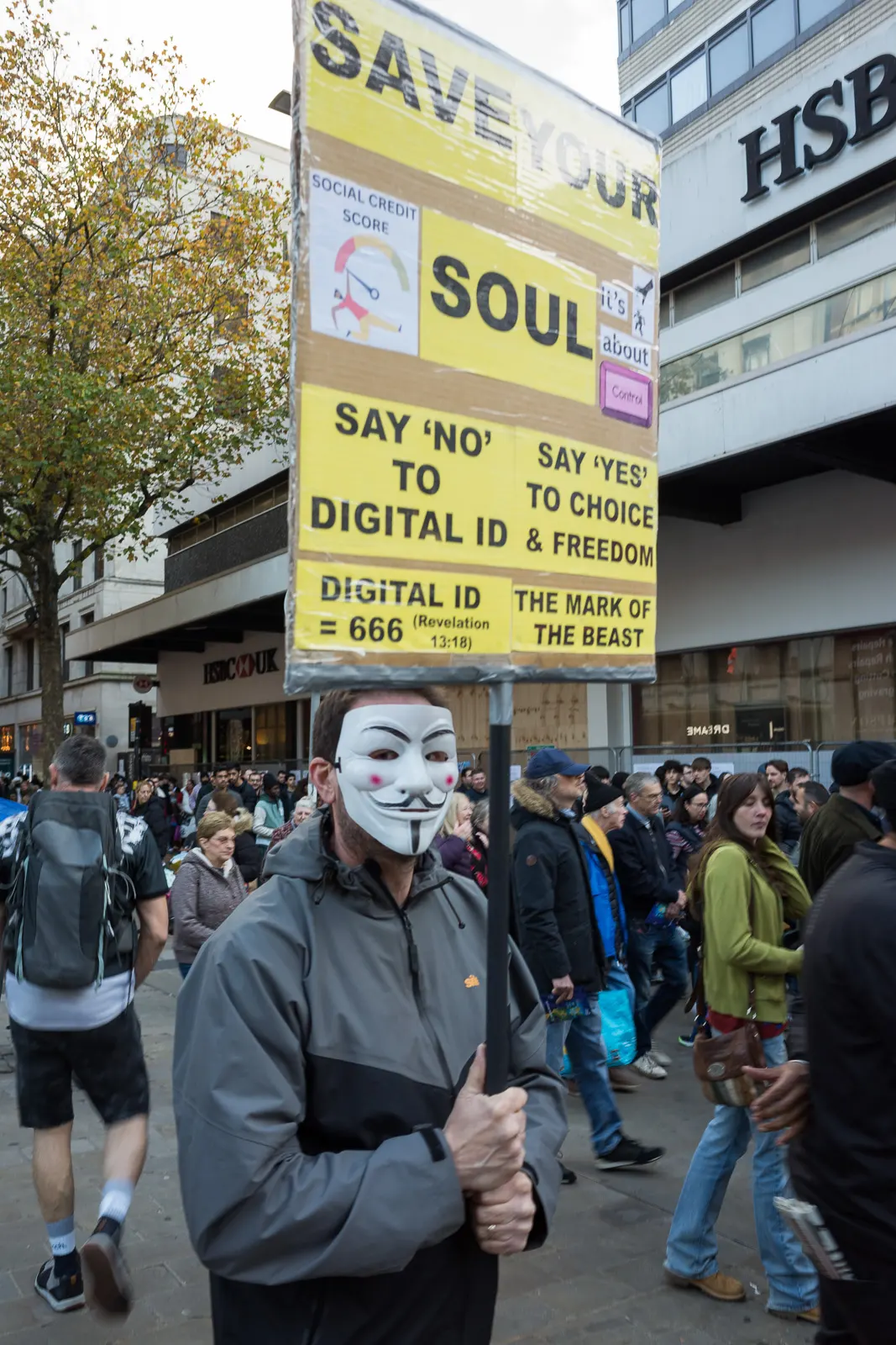 A protestor in a Guy Fawkes mask holds a sign reading, "Say 'No' to Digital ID"