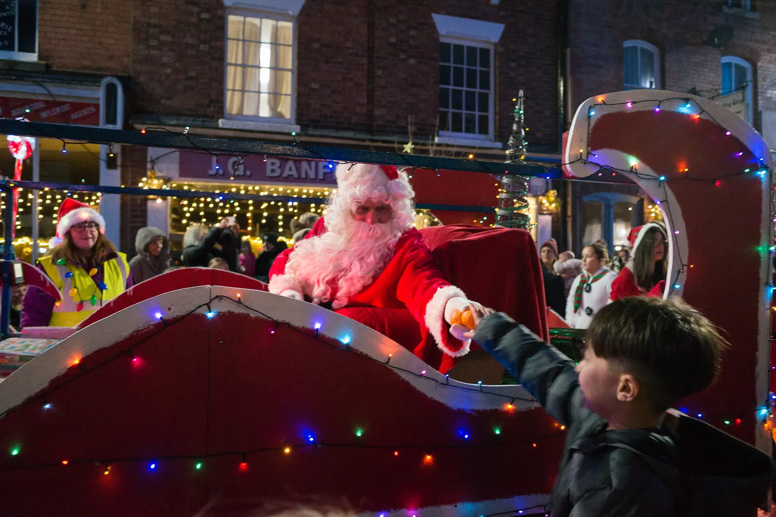 Santa hands out oranges to children as the parade passes by