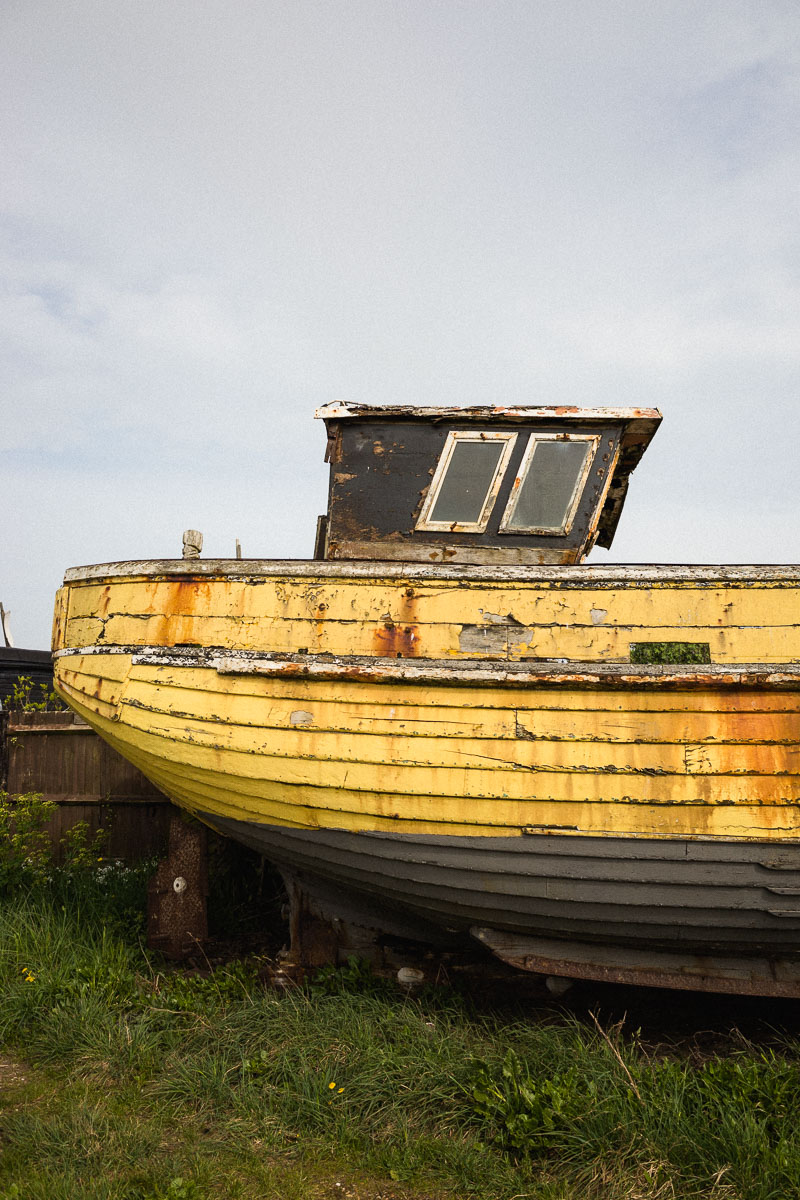 Peeling yellow paint on a weathered wooden fishing boat on Hastings Beach—ideal for abandonment photography