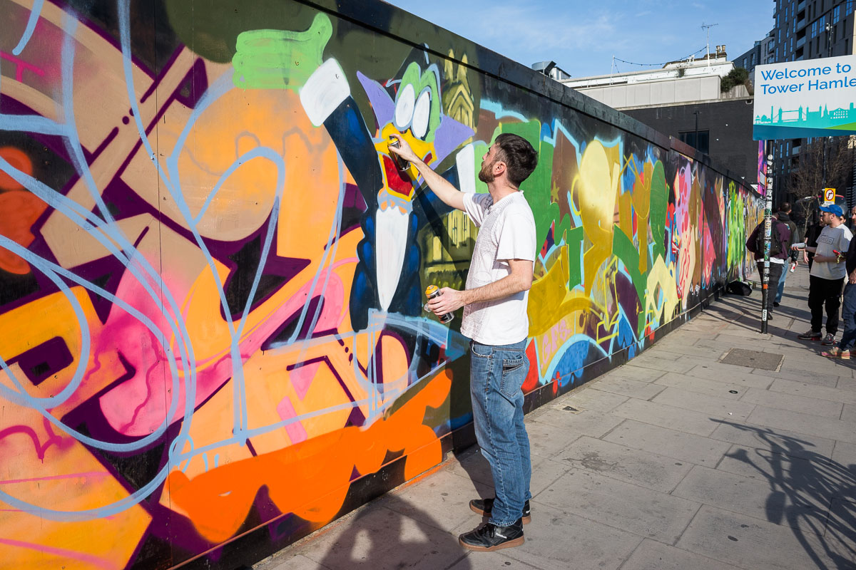 A graffiti artist caught spray can in hand, working on a wall in Brick Lane