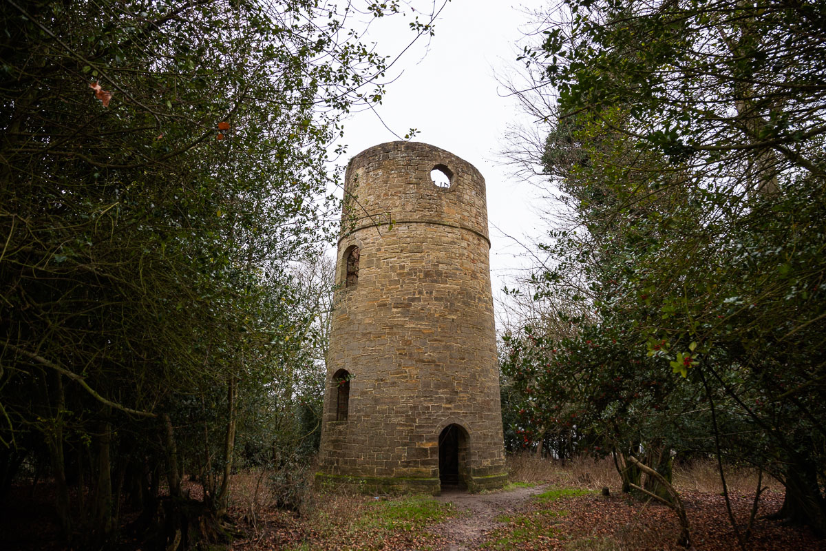 A round stone tower in Brightling woods, one of Fuller’s Follies, partially hidden among trees